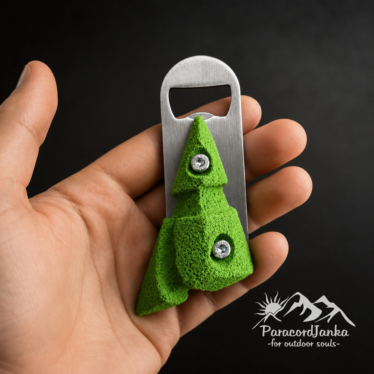 A hand holding a green climbing hold bottle opener with a textured surface and metal opener blade against a dark background.