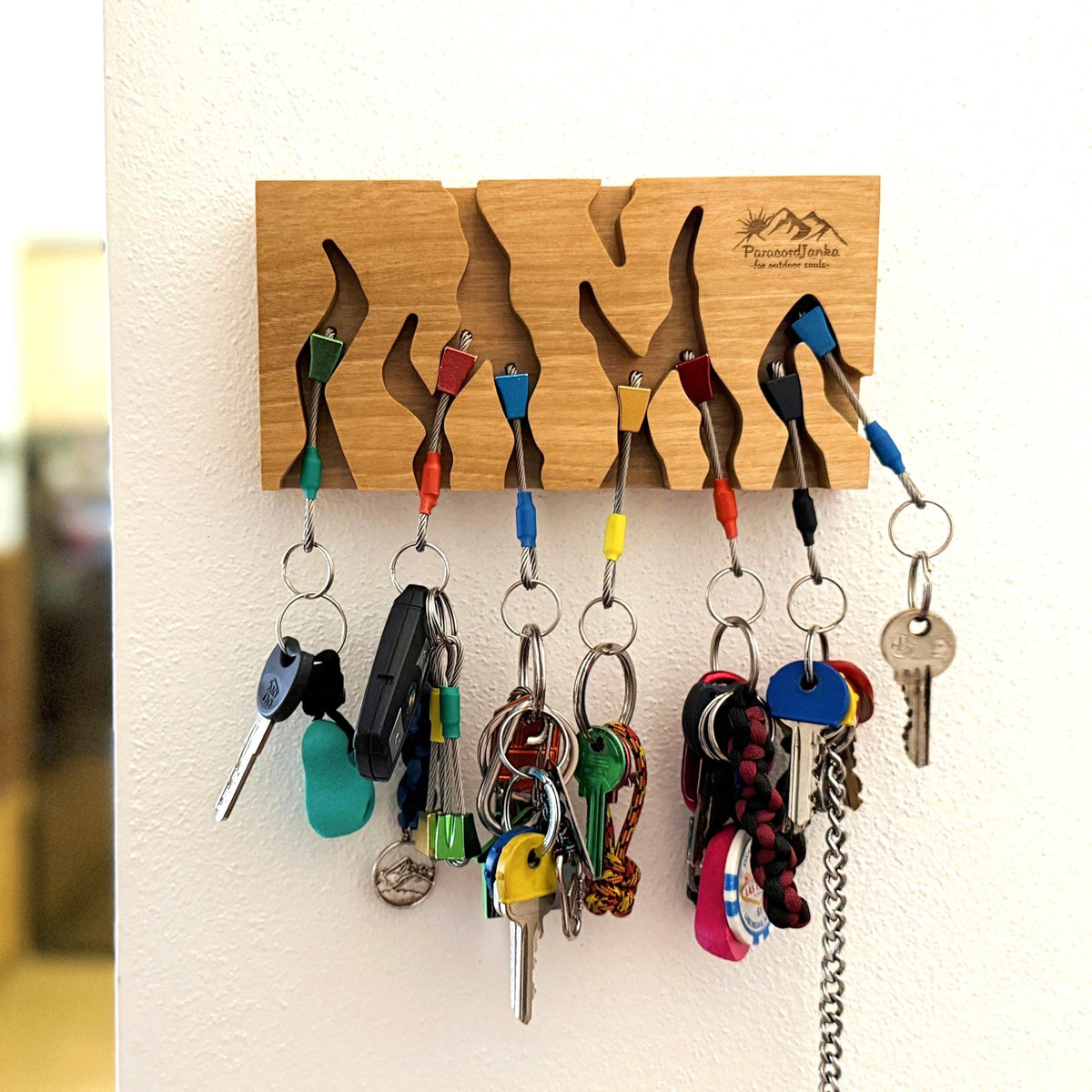 Wooden key holder with multiple hooks holding various keys on a white wall.