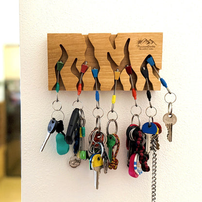Wooden key holder with multiple hooks holding various keys on a white wall.