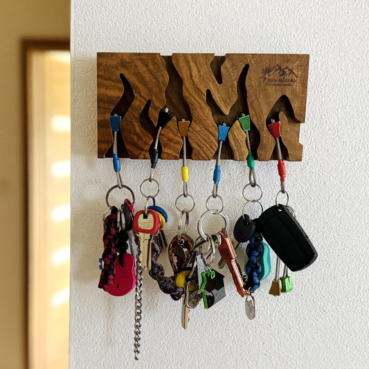 Wooden key holder with various keys hanging on it against a white wall.