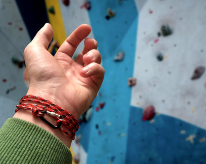 Hand with red climbing bracelet on a climbing wall background