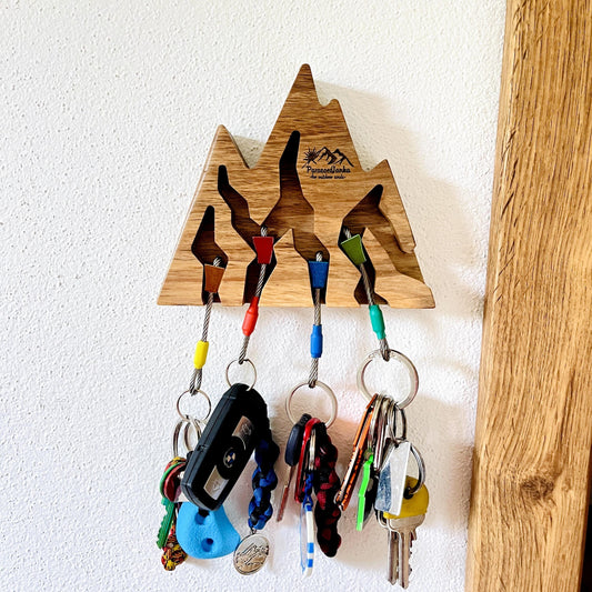Wooden key holder shaped like mountains with keys attached on a white wall.