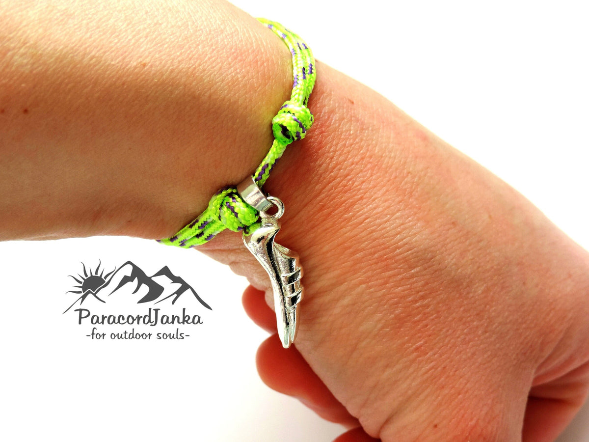 Hand wearing a green paracord bracelet with a silver charm, branded 'ParacordJanka'.