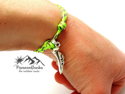 Hand wearing a green paracord bracelet with a silver charm, branded 'ParacordJanka'.