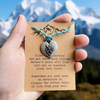 Necklace with heart-shaped pendant on a card held against a mountainous background