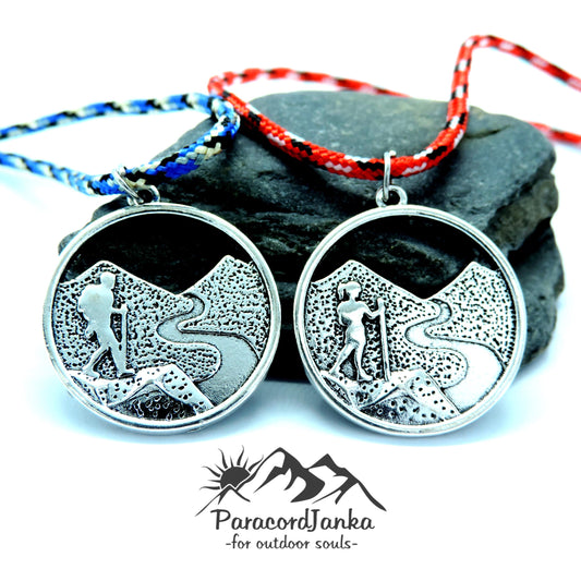 Two silver necklaces with hiking designs on a stone surface, featuring the brand 'ParacordJanka'.