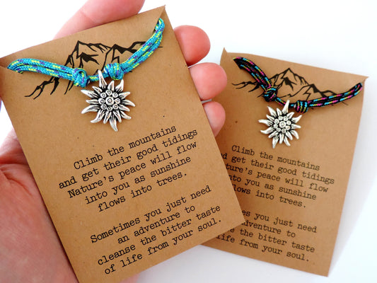 A hand holding an Edelweiss Mountain Necklace Gift for Hiker mounted on a craft paper presentation card.