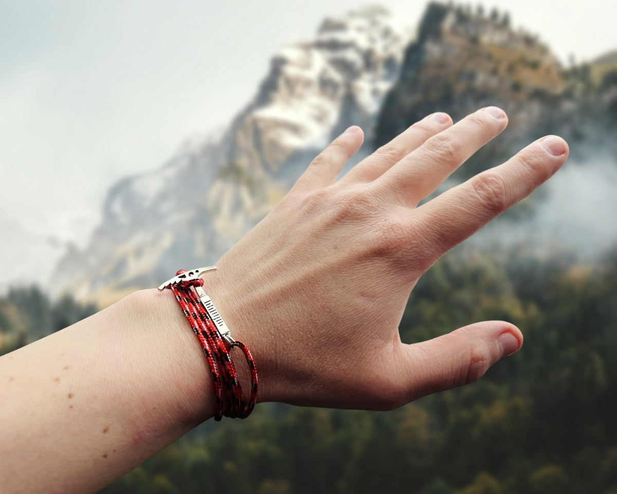 Hand wearing a red climbing bracelet with a mountainous background