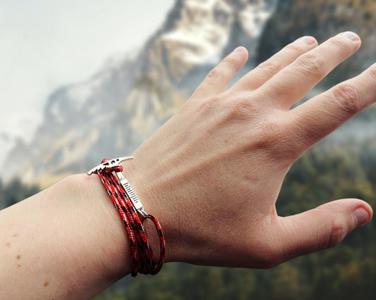 Hand wearing a red climbing bracelet with a mountainous background