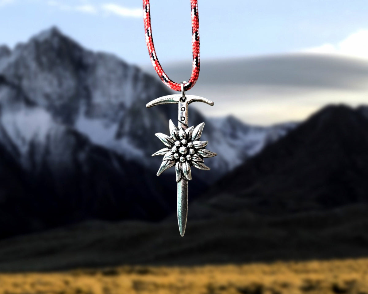 Silver climbing pendant with red cord against a mountainous landscape