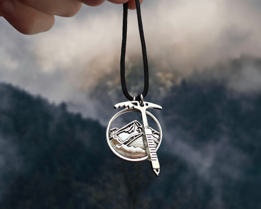 Silver pendant on a black cord held against a mountainous landscape
