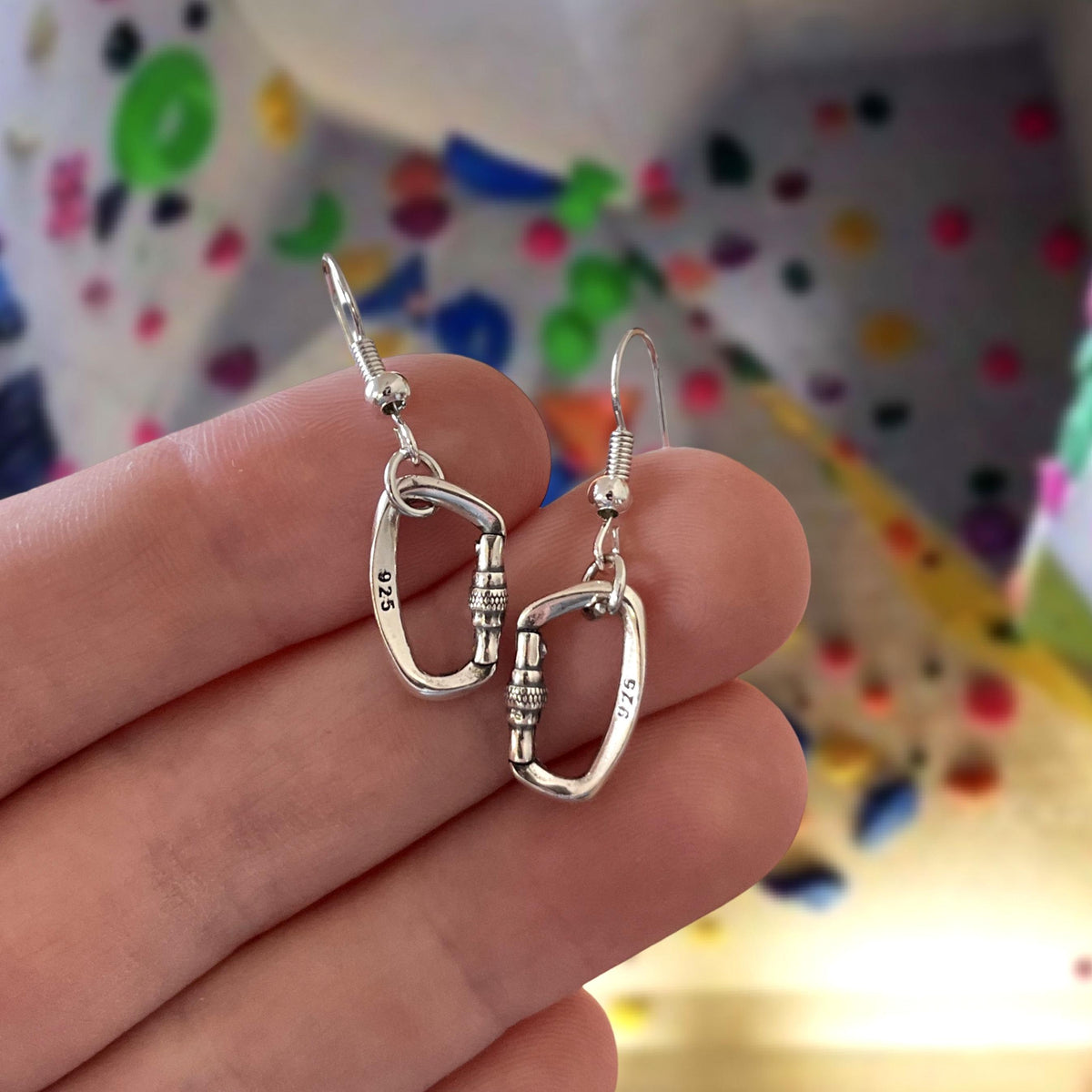 Silver earrings held between fingers with a colorful polka dot background