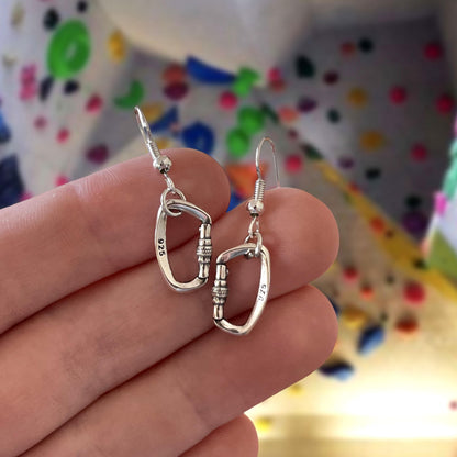 Silver earrings held between fingers with a colorful polka dot background