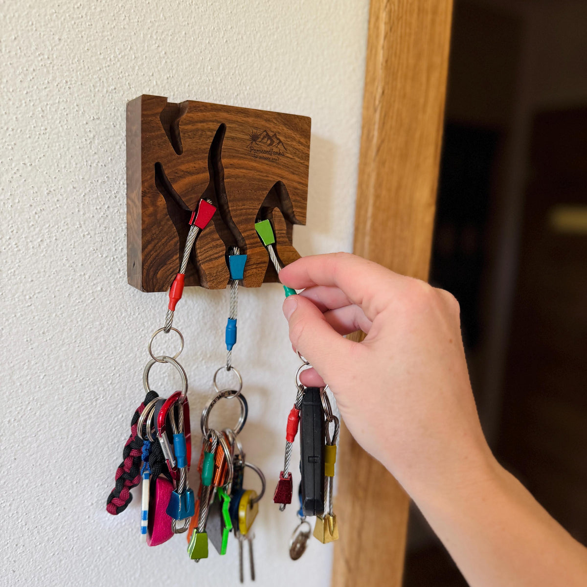 Wooden key holder with colorful keys attached, mounted on a wall.