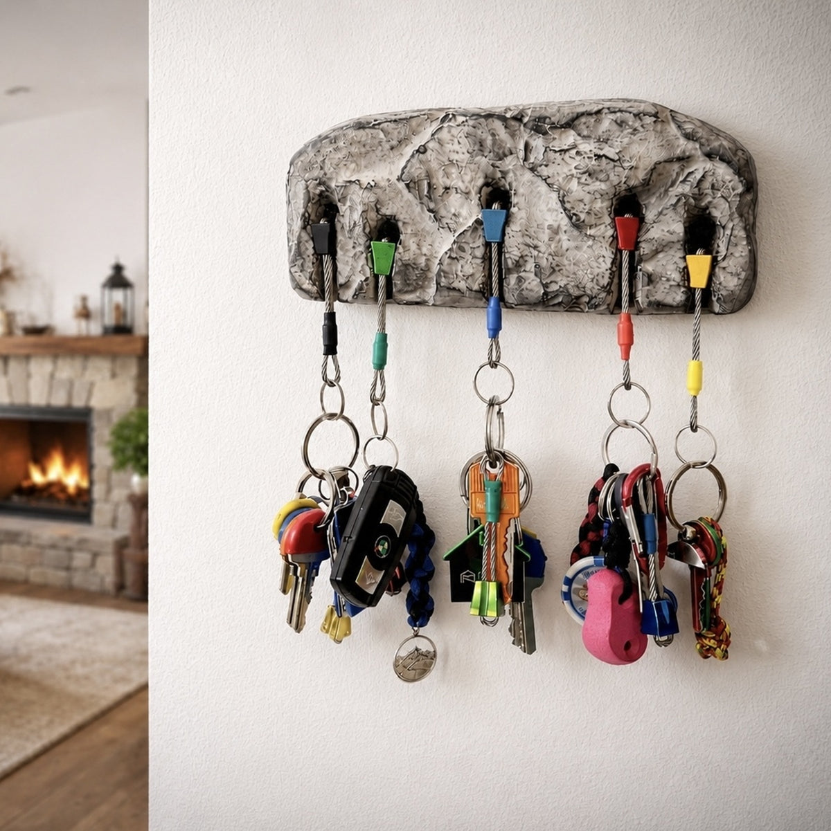 A textured gray stone-look key holder mounted on a white wall, holding several colorful keychains and keys in a home interior setting.