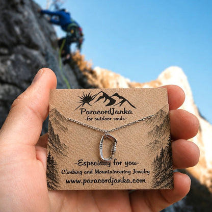 Silver Carabiner Climbing Necklace Gift Jewelry displayed on a card held by a hand with a climber in the background.