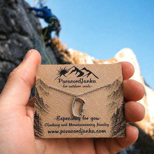 Silver Carabiner Climbing Necklace Gift Jewelry displayed on a card held by a hand with a climber in the background.