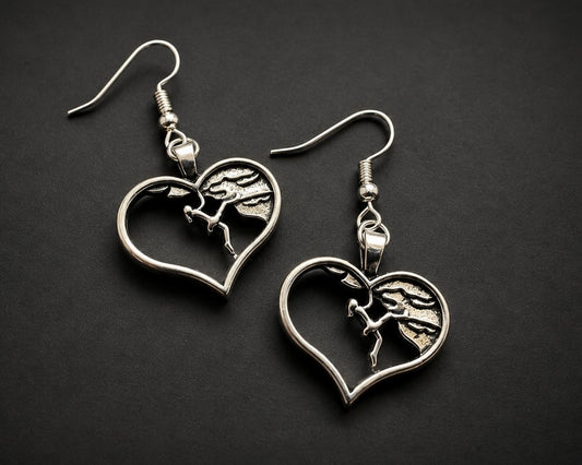 A pair of silver-toned drop earrings featuring heart-shaped cutouts with a detailed horse and rider motif in the center, displayed on a dark textured background.