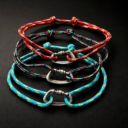 Four braided cord bracelets with silver-toned carabiner-style clasps, arranged in a stack on a dark background. The cords are multicolored, featuring red, blue, green, and purple threads.