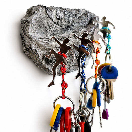 A wall-mounted key holder featuring three running athlete silhouettes attached to a gray rock plaque, with colorful braided cords and multiple keys hanging below on metal key rings against a white background.