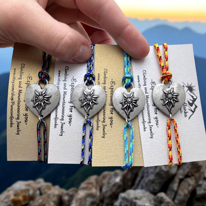 Four colorful friendship bracelets with a silver heart charm featuring an edelweiss flower. The bracelets are made with paracord and have the text "Esp for you" on the card.