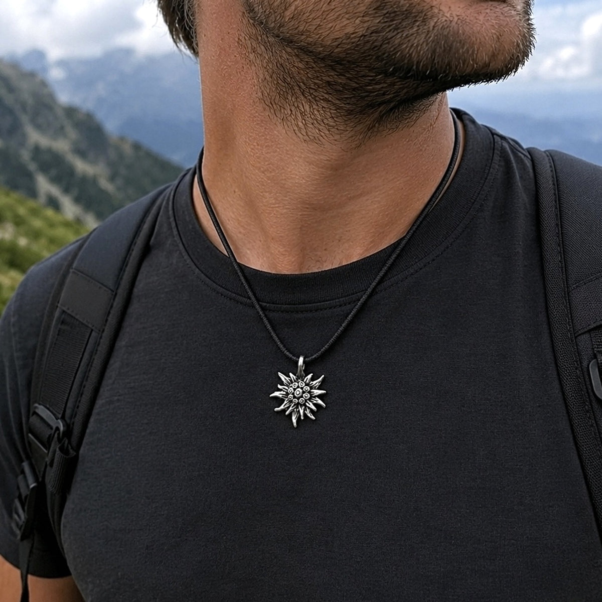 A man wearing an Edelweiss Mountain Necklace Gift for Hiker outdoors with mountain peaks behind him.