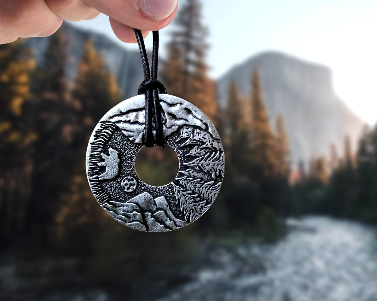 A hand holding up a Hiking Mountain Necklace Gift with a mountain peaks background.