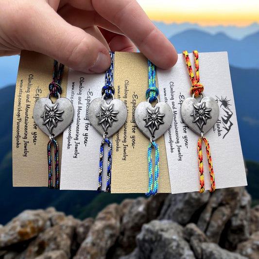 May include: Four colorful friendship bracelets with a silver heart charm featuring an edelweiss flower. The bracelets are made with paracord and have the text "Esp for you" on the card.