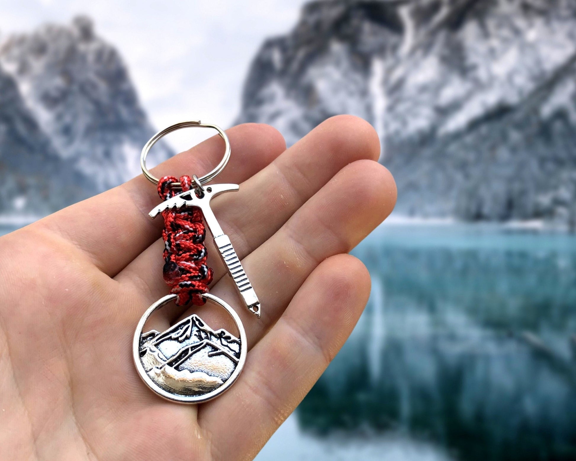 May include: A silver keychain with a red and black braided cord. The keychain features a small ice axe charm and a round charm with a mountain silhouette.