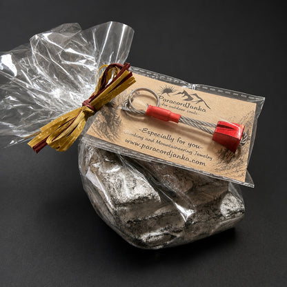 A small jewelry keychain with red end caps and a metal ring, attached to a kraft paper card and wrapped in clear plastic, placed on top of a silver rock against a dark background.