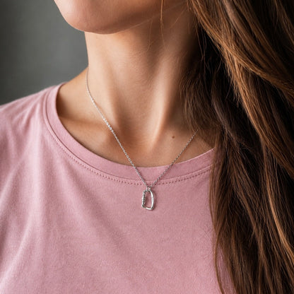 A close-up of a woman wearing a delicate silver chain necklace with a small, openwork silver pendant, paired with a soft pink crewneck t-shirt.