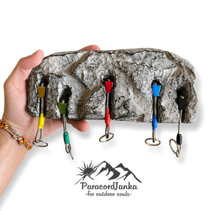 A hand holds a rock-climbing-style wall hook rack with six metal hooks in different colored sleeves, shown against a white background with the Paracord Janka logo below.