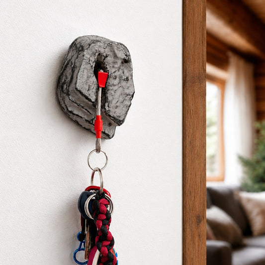 A gray rock-shaped wall hook with red accents holds a set of keys and a red strap in a home interior setting.