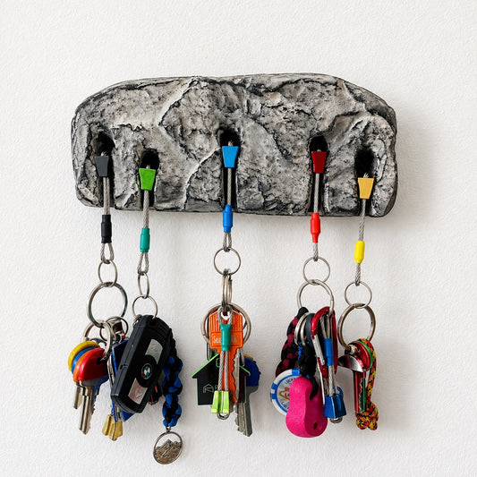 A textured gray stone-look key holder with five colorful hooks holding various keys and accessories, mounted on a plain white wall.