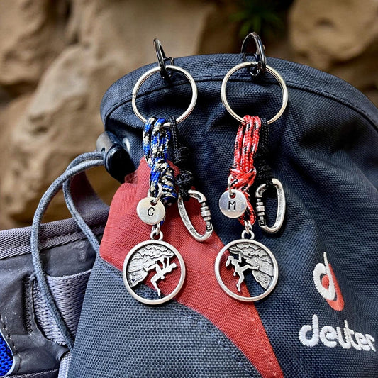 Two keychains with charms hanging from a backpack against a natural stone background