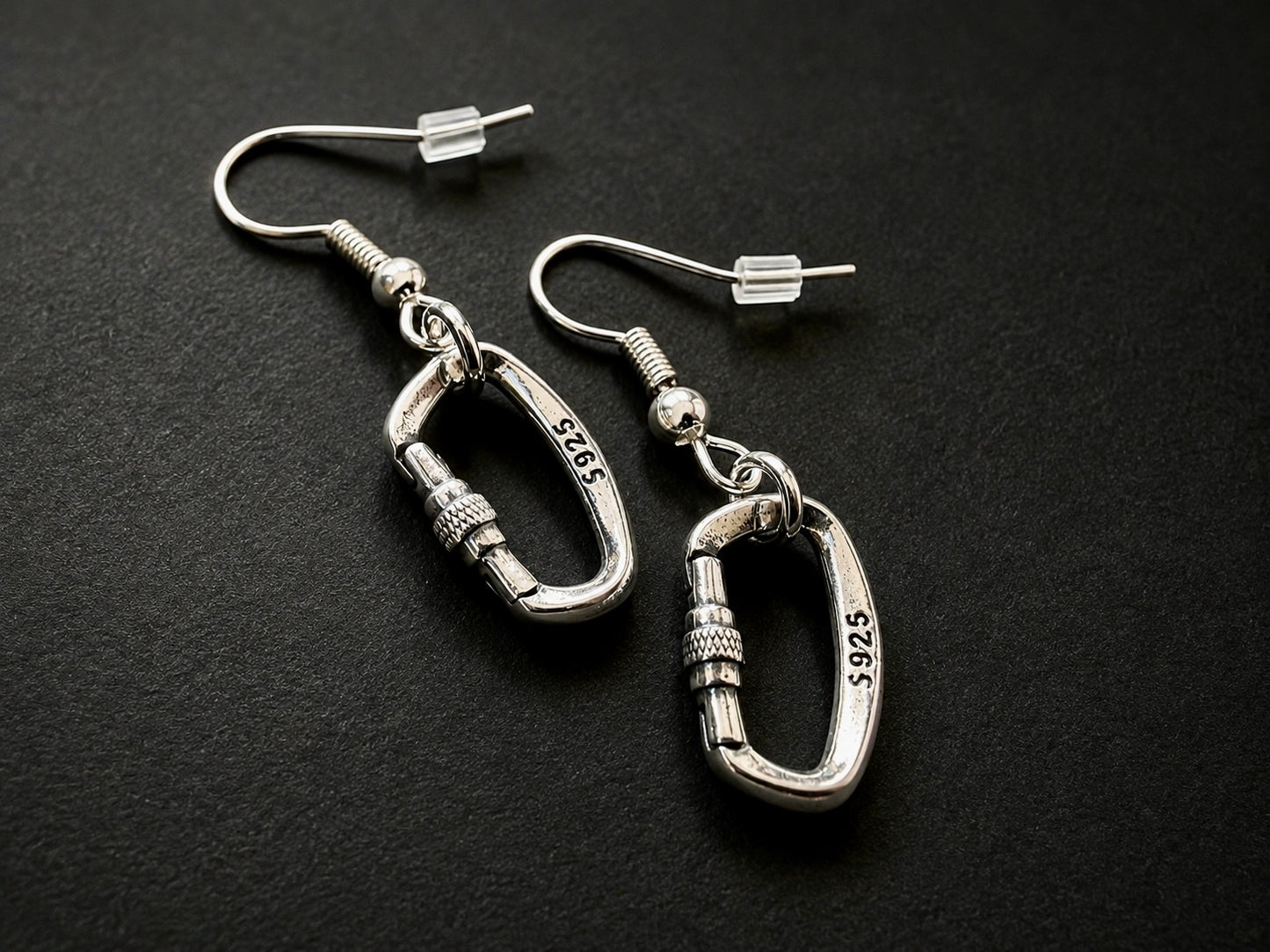 Silver Openable Climbing Earrings Jewelry A pair of silver carabiner dangle earrings with 14k yellow gold-plated hooks, displayed on a dark textured background. The carabiners are engraved with '14K 5925'.