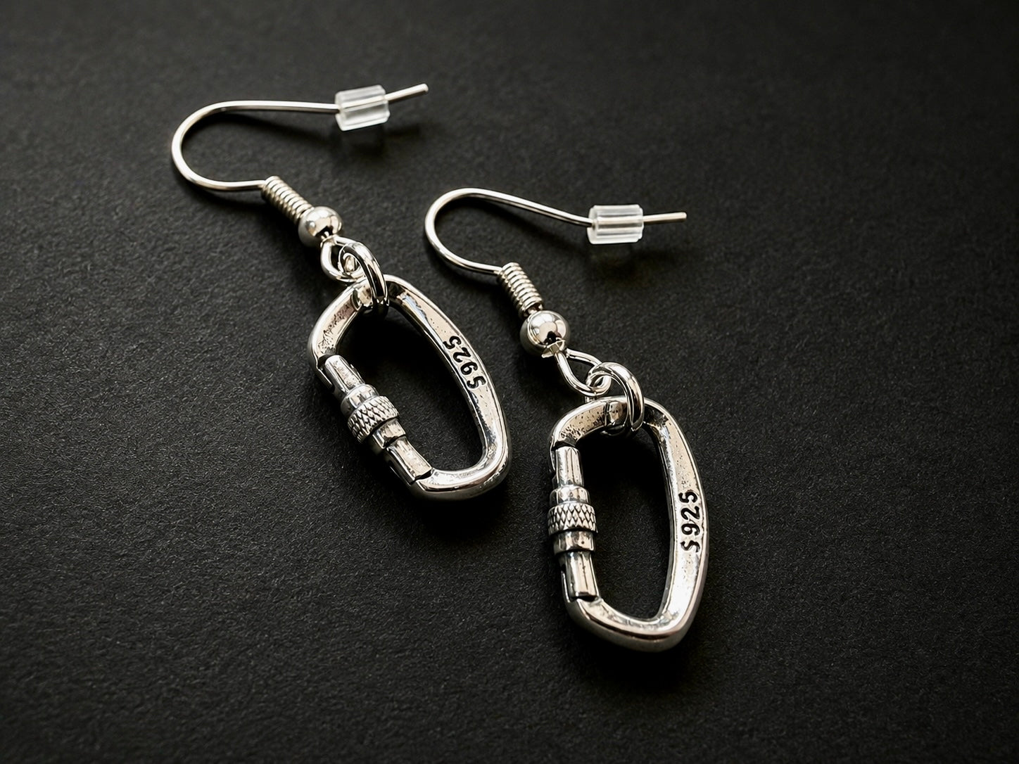 Silver Openable Climbing Earrings Jewelry A pair of silver carabiner dangle earrings with 14k yellow gold-plated hooks, displayed on a dark textured background. The carabiners are engraved with '14K 5925'.