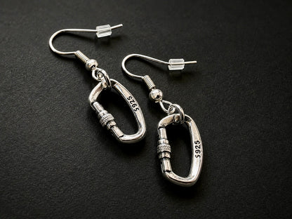 Silver Openable Climbing Earrings Jewelry A pair of silver carabiner dangle earrings with 14k yellow gold-plated hooks, displayed on a dark textured background. The carabiners are engraved with '14K 5925'.