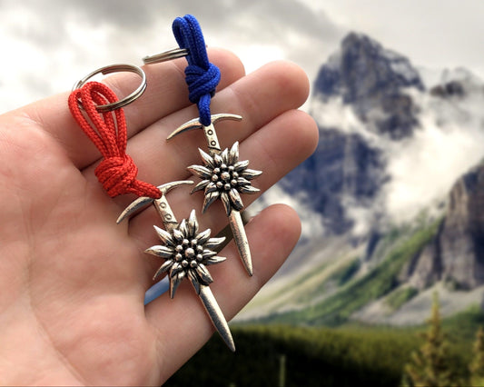 Two silver climbing keychains with a ice axe design and a flower charm. The keychains are attached to red and blue cords.